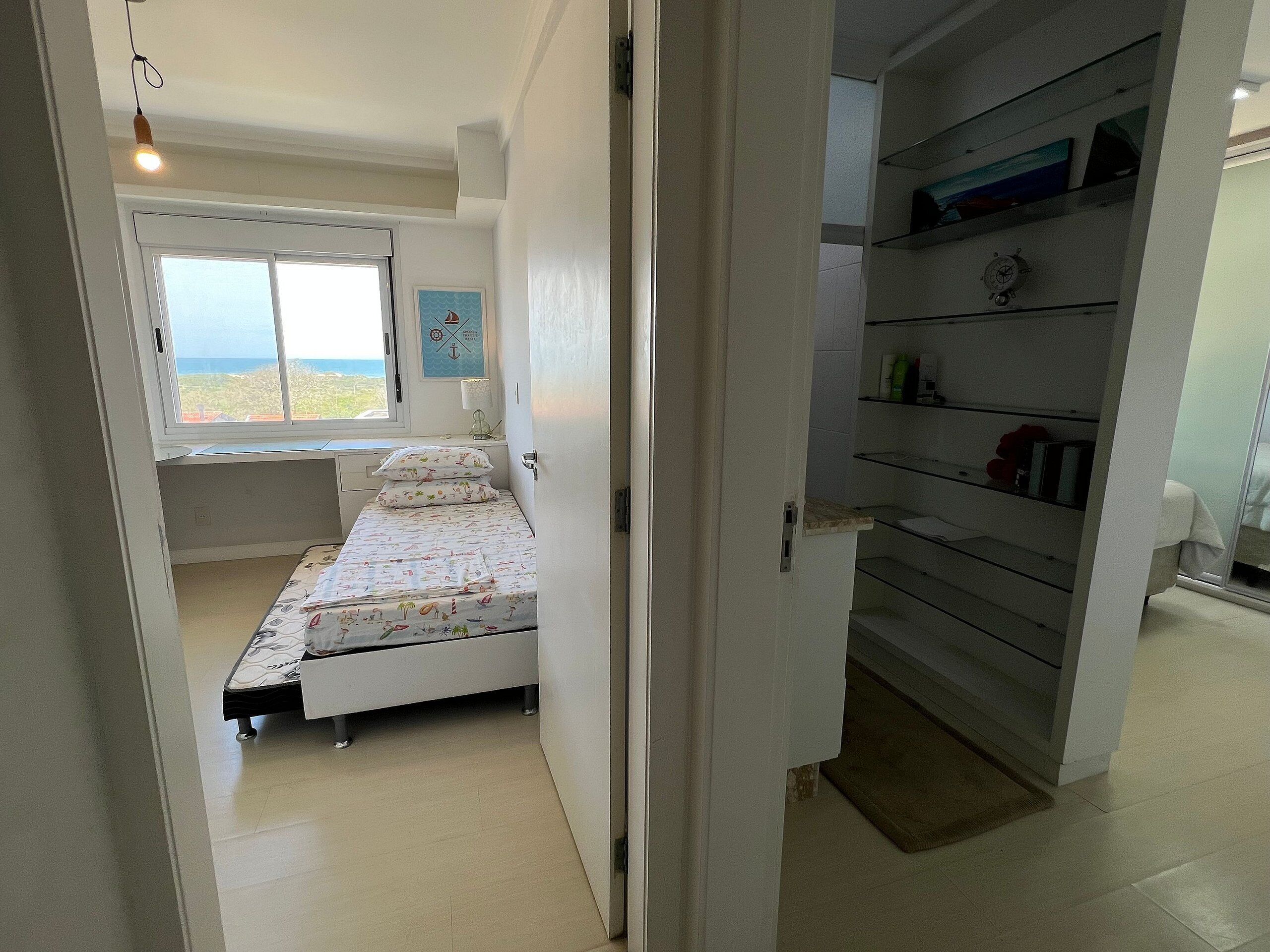 A bedroom with a bed, a window, a desk, and a shelving unit.