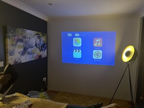 A room with a projection screen displaying app icons, a painting on the wall, and a floor lamp.