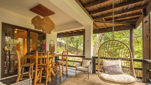 A wooden deck with wicker furniture, a hanging chair, and a view of greenery.