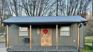 A small, single-story cabin with a dark gray exterior, a wooden door, and a red heart decoration. - Perfect cozy bungalow for a weekend away or a week fishing🐟 (Sale Creek)