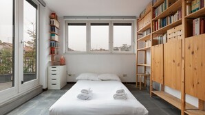 A bedroom with a large window, a bed with towels, a bookshelf, and a white dresser. - GuestHost - APT with large terrace - Calvairate neighborhood (Milano)