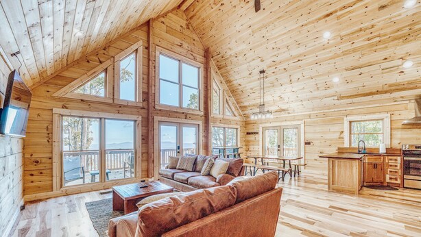 A spacious cabin with a high ceiling, large windows, a cozy living area with a sofa and coffee table, and a kitchen area. - Family Retreat in this Gorgeous Log Cabin overlooking the Arkansas Grand Canyon! (Jasper)
