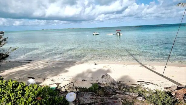 A beach with clear turquoise water, a sandy shore, and a fishing rod. - Bayview Cottage (Staniel Cay)
