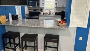 A kitchen with a granite countertop, stainless steel appliances, and a window with blinds. - Bayview Cottage (Staniel Cay)
