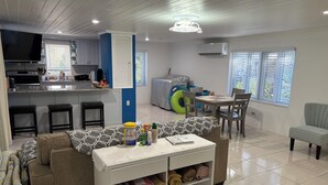 A modern living room with a sofa, a coffee table, and a dining area with a table and chairs. - Bayview Cottage (Staniel Cay)