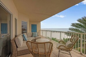 A balcony with a wicker sofa, chairs, and a view of the beach.