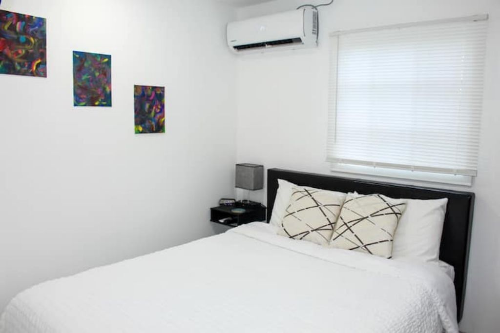 Un dormitorio con cama, paredes blancas y tres cuadros abstractos.