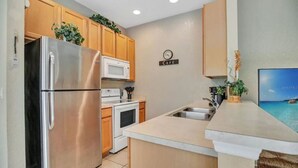 A modern kitchen with stainless steel appliances, wooden cabinets, and a 'CAFE' sign on the wall.