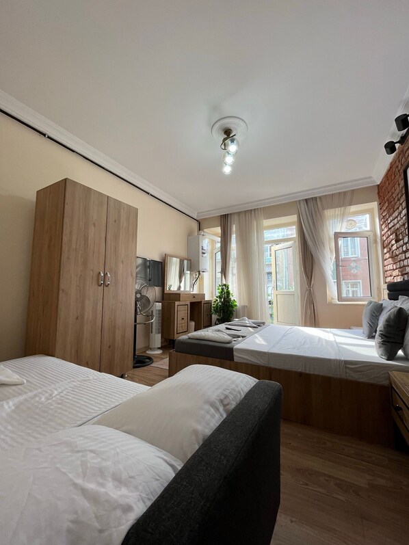 Quarto com duas camas, guarda-roupa de madeira, escrivaninha com cadeira, ventoinha e janela com cortinas.