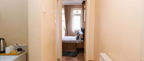 A narrow hallway leading to a bedroom with a bed, a radiator, and a window with curtains.
