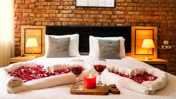 Habitación de hotel con pared de ladrillo, cama con ropa blanca, dos lámparas de noche y una obra de arte enmarcada sobre la cama.