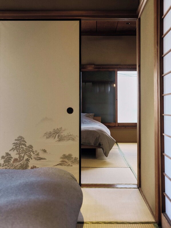 A traditional Japanese room with tatami flooring, a bed with a gray blanket, and a shoji screen door.