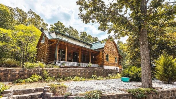 A log cabin with a porch, stone steps, and a gravel driveway. - Dragonfly Meadows Log Cabin (Stoutland)