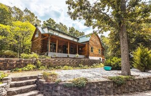 A log cabin with a porch, stone steps, and a gravel driveway. - Dragonfly Meadows Log Cabin (Stoutland)