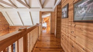A wooden interior corridor with a wooden railing, wooden walls, and a ceiling with wooden beams. - Dragonfly Meadows Log Cabin (Stoutland)