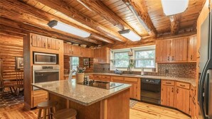 A kitchen with wooden cabinets, a granite countertop island, and a built-in oven. - Dragonfly Meadows Log Cabin (Stoutland)