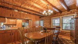 A wooden cabin interior with a dining table, chairs, and a chandelier. - Dragonfly Meadows Log Cabin (Stoutland)