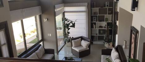 A spacious living area with a high ceiling, large windows, and a variety of seating options including a sofa and a chair.