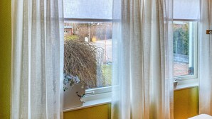 A window with sheer curtains, a view of a yard with a tree and a building in the background. - Amazing apartment in Färjestaden (Färjestaden)