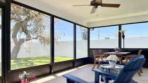 Eine sonnendurchflutete Terrasse mit Tisch und Stühlen, großen Fenstern und einem Deckenventilator.