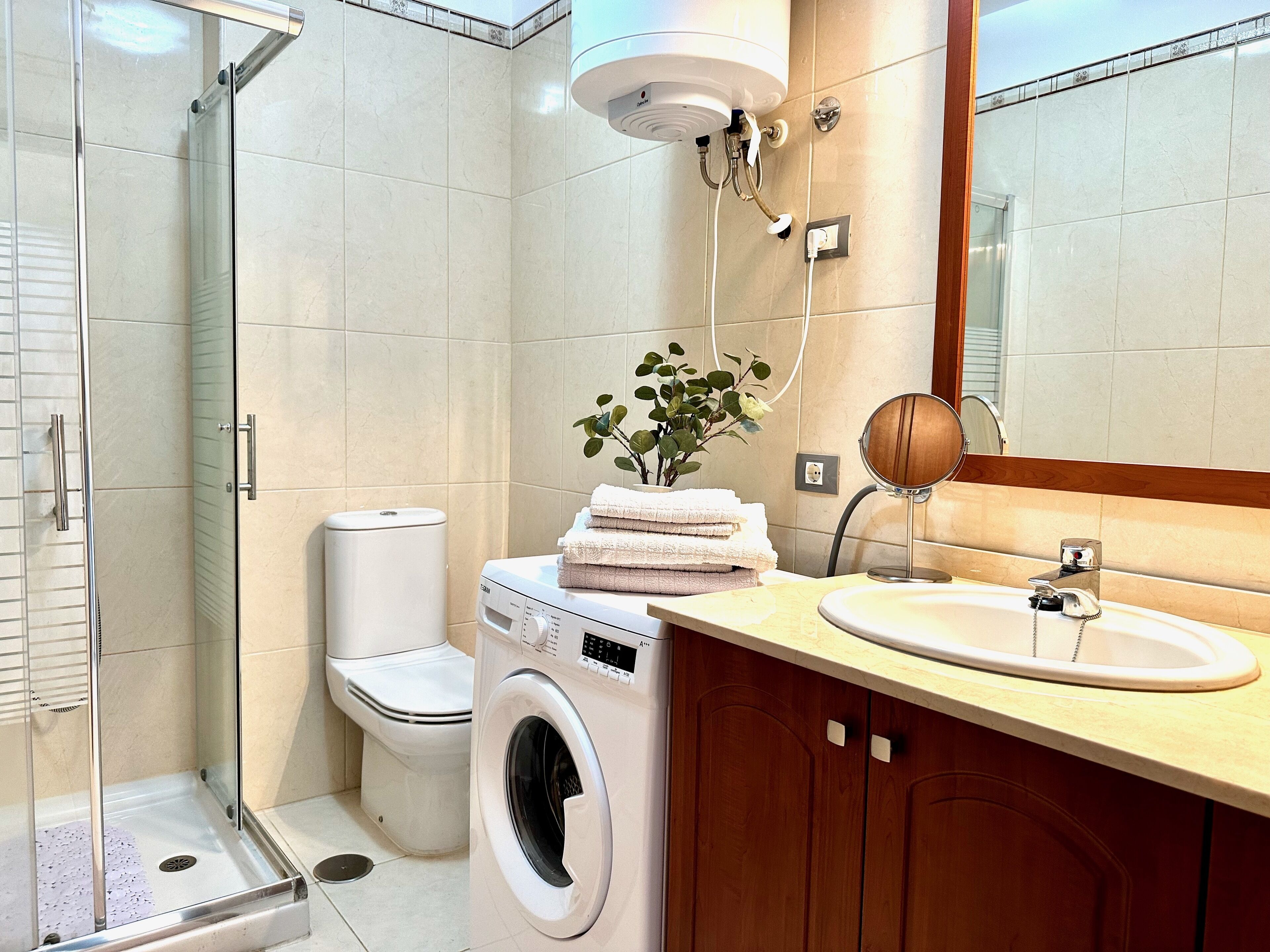 Un baño con ducha de vidrio, inodoro, lavadora y lavamanos con espejo.