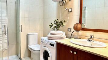 Un baño con ducha de vidrio, inodoro, lavadora y lavamanos con espejo.