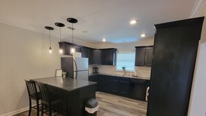 A modern kitchen with dark cabinetry, a central island with seating, and a black refrigerator. - 2bed/2bath Cottage in Downtown Houma. 30+ day stays welcome. (Houma)