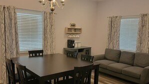 A dining area with a dark wooden table and chairs, a sofa, and a chandelier. - 2bed/2bath Cottage in Downtown Houma. 30+ day stays welcome. (Houma)