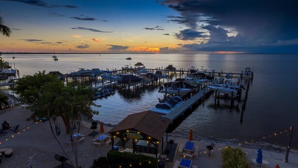 A marina with boats docked, a beach area with lounge chairs, and a sunset view. - Sunsets and Turtles – Key Largo Moon Bay Condo – Boat Slip/Lift Optional (Key Largo)