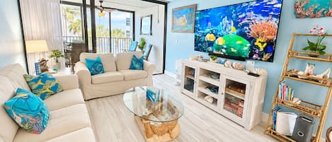 A living room with a beige sofa, a glass coffee table, a TV, and a bookshelf.