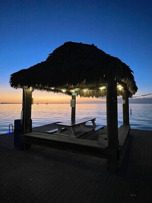 A thatched-roof structure with a bench, located on a dock with a view of calm water and boats in the distance. - Sunsets and Turtles – Key Largo Moon Bay Condo – Boat Slip/Lift Optional (Key Largo)