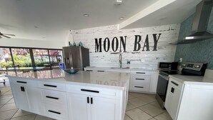 A modern kitchen with white cabinetry, a large island, stainless steel appliances, and a backsplash with the text "MOON BAY". - Sunsets and Turtles – Key Largo Moon Bay Condo – Boat Slip/Lift Optional (Key Largo)