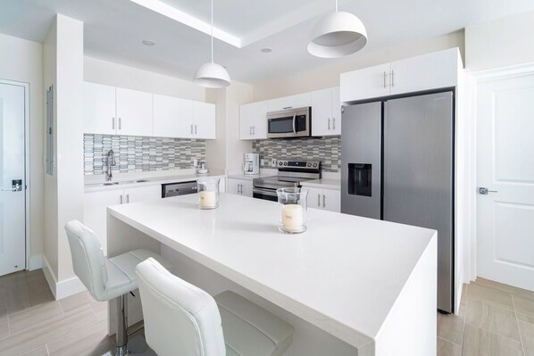 Una cocina moderna con muebles blancos, electrodomésticos de acero inoxidable y una isla central con taburetes de bar.