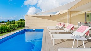 A pool area with lounge chairs and tables, a clear blue sky, and a view of the ocean. - Incredible villa, beach club access- Whitehaven  (2 bed) (Westmoreland)