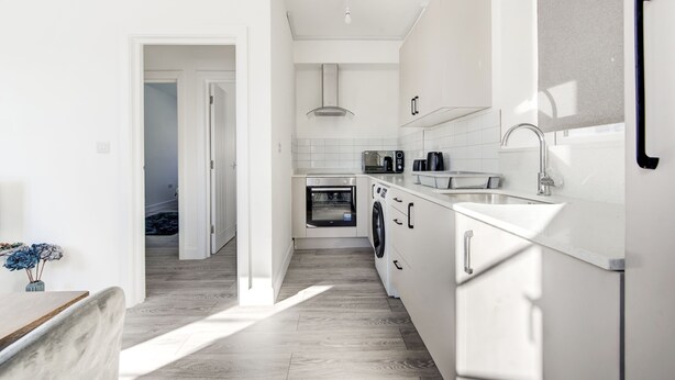 Una cocina moderna con armarios blancos, horno integrado y lavadora.