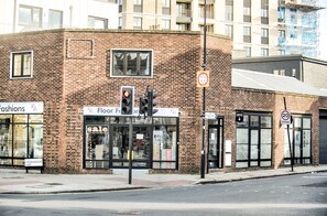 Un edificio de ladrillo con escaparate que dice "Fashions" y un letrero que indica "Se vende piso".