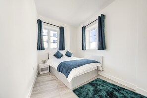 A bedroom with a bed, nightstand, and a window with curtains. - Modern 2-Bedroom Apartment in Vibrant Brixton - Perfect for City Explorers! (London)