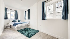 Un dormitorio con cama, mesita de noche, ventana con cortinas y vistas al exterior.