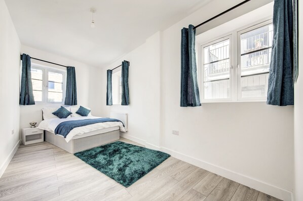 Un dormitorio con cama, mesita de noche, ventana con cortinas y vistas al exterior.
