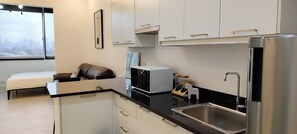A modern kitchen with white cabinets, a black countertop, a stainless steel refrigerator, and a built-in microwave. - Condominium in Kamuning (Lungsod Quezon)