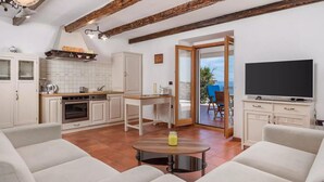 A modern kitchen with white cabinets, a dining area with a round table, and a TV in a white cabinet. - Amazing home in Labin - Rabac (Labin - Rabac)