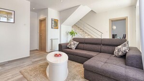 A modern living room with a grey sofa, a round white coffee table, and a staircase leading to an upper floor. - Awesome home in Liznjan (Liznjan)