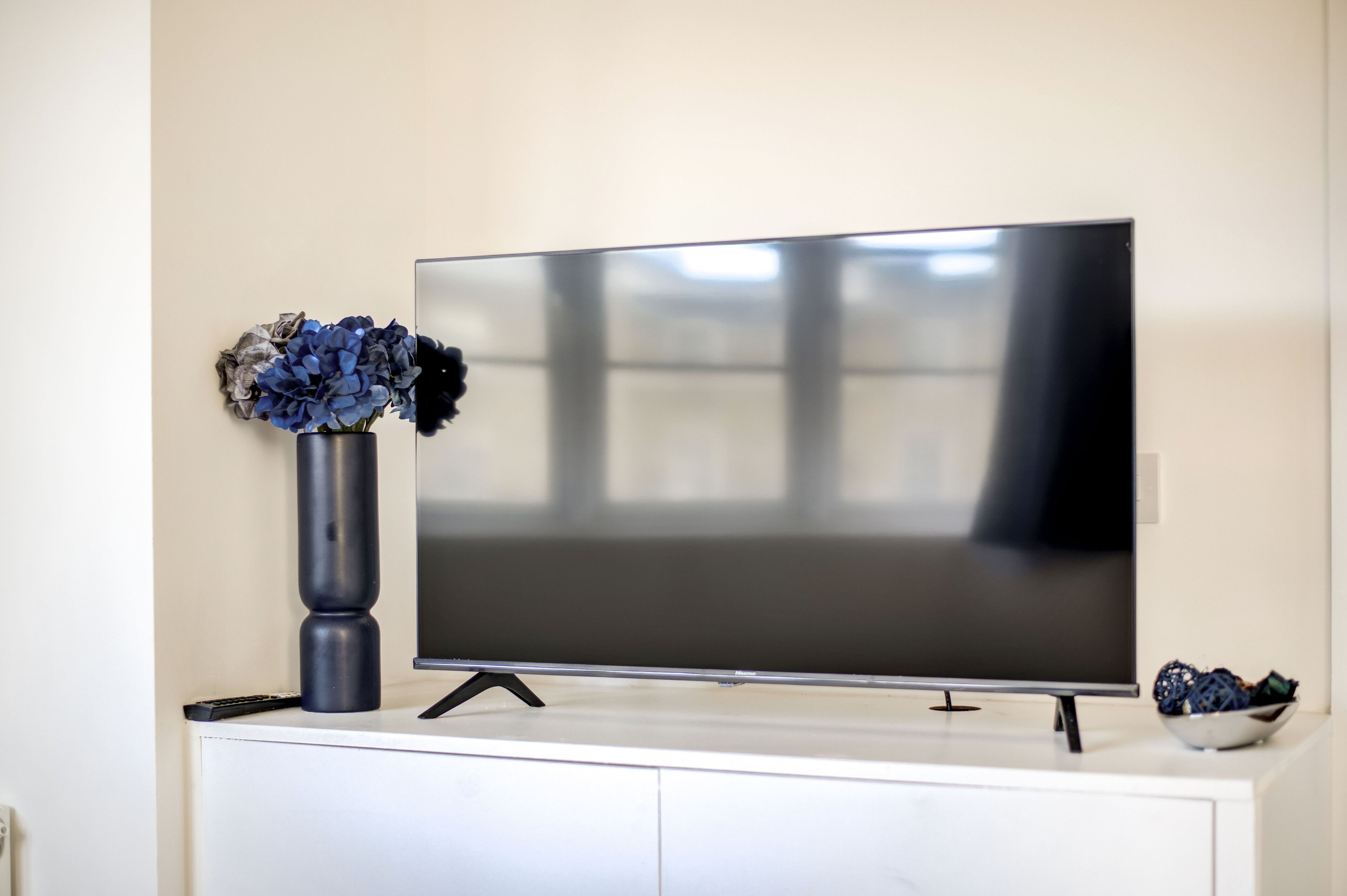 A flat-screen TV on a white cabinet with a vase of flowers to the left.