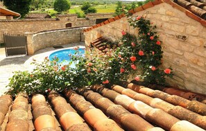 Un bâtiment en pierre doté d’une piscine, entouré d’un jardin où s’épanouissent des rosiers.