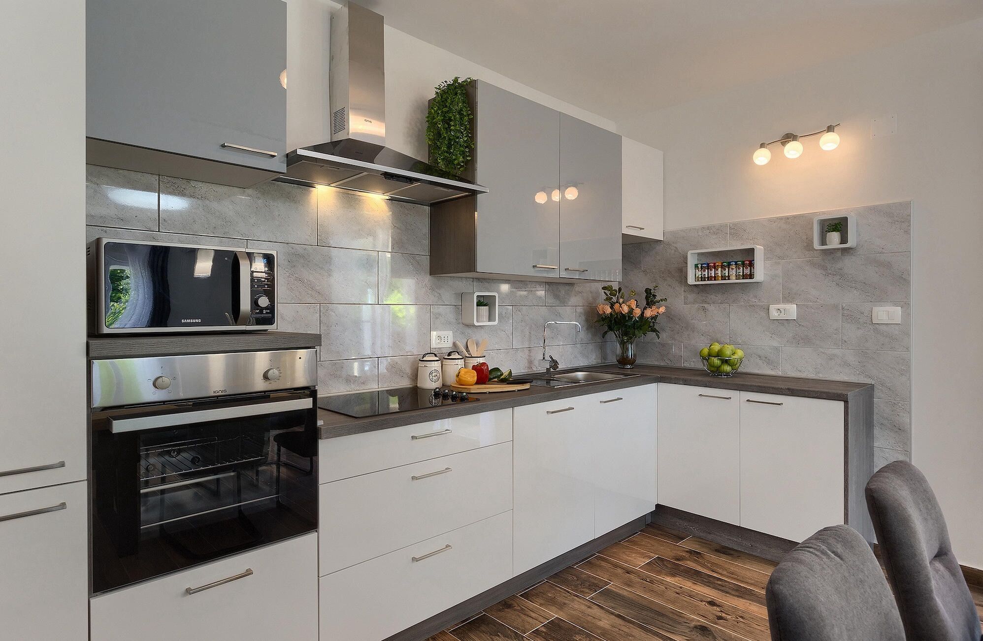 A modern kitchen with built-in appliances, a grey tiled backsplash, and a wooden floor.