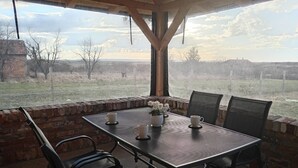 Une terrasse extérieure avec une table et des chaises, un mur en briques et une vue sur un champ verdoyant.