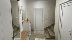 Un couloir avec un banc en bois, une porte et une petite plante accrochée au mur.