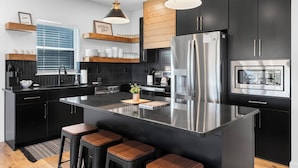 A modern kitchen with black cabinetry, stainless steel appliances, and wooden bar stools.