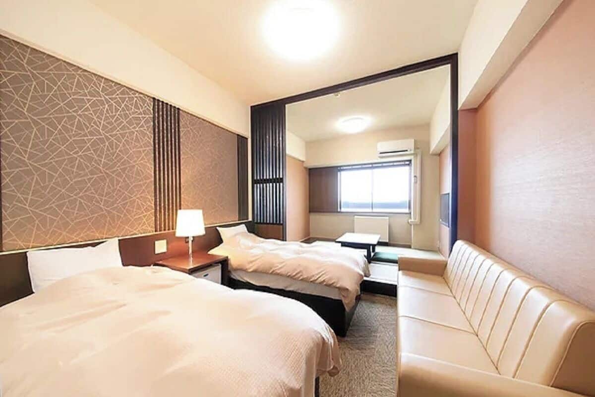 A hotel room with two beds, a sofa, a mirror, and a window.