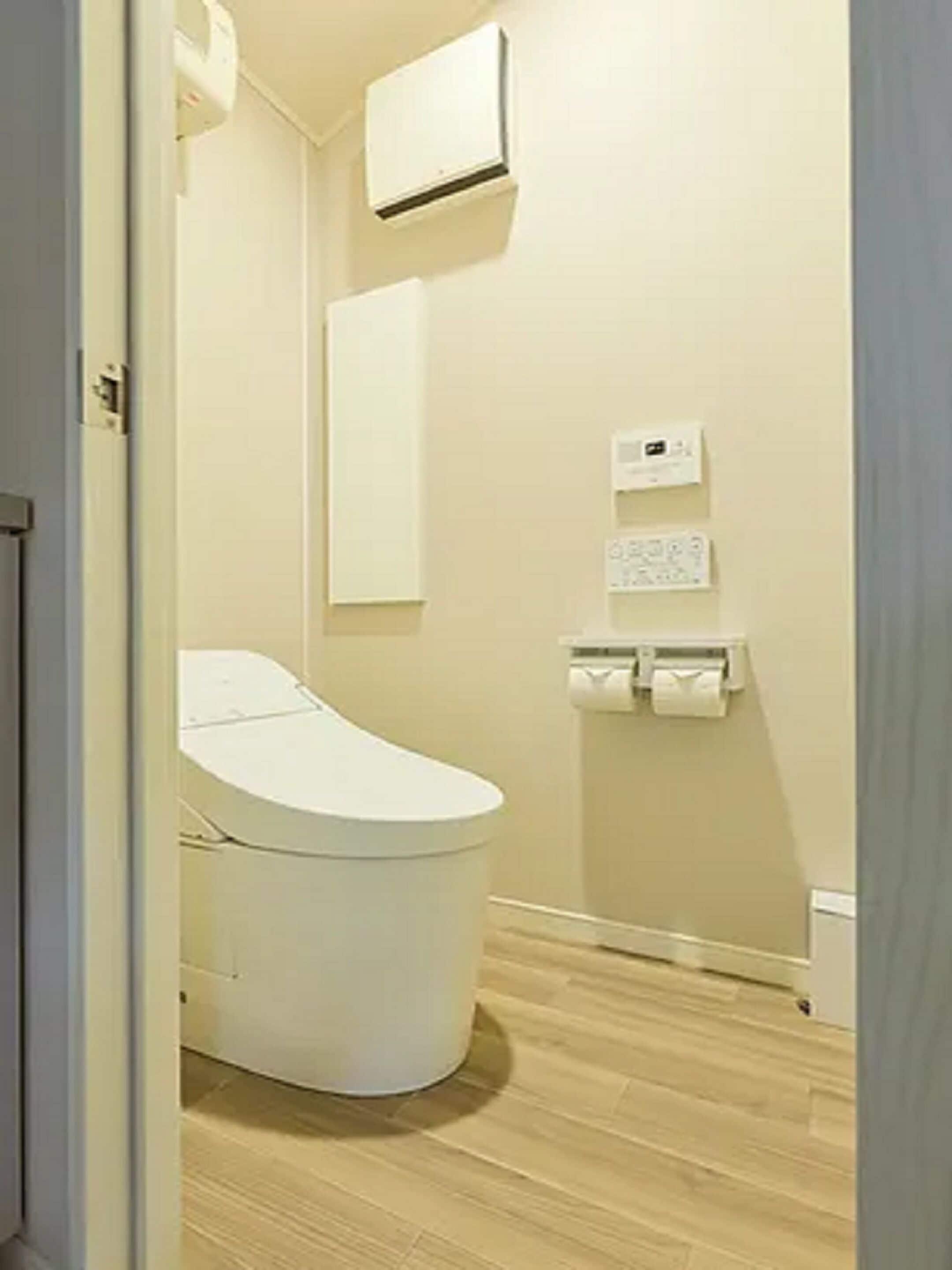 A bathroom with a toilet, a wall-mounted air conditioner, and a paper towel dispenser.